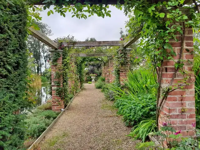 Brick pergola with climbing plants over a gravel path, breaking a long garden into distinct sections