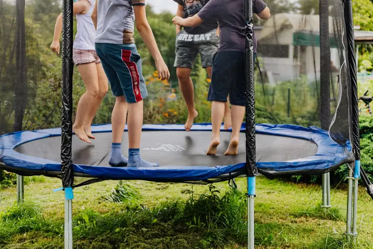 Children jumping on a netted trampoline set on grass in a family back garden