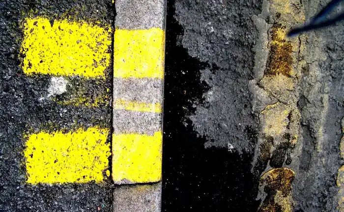 Close view of double yellow lines painted along the edge of a road beside a worn kerb