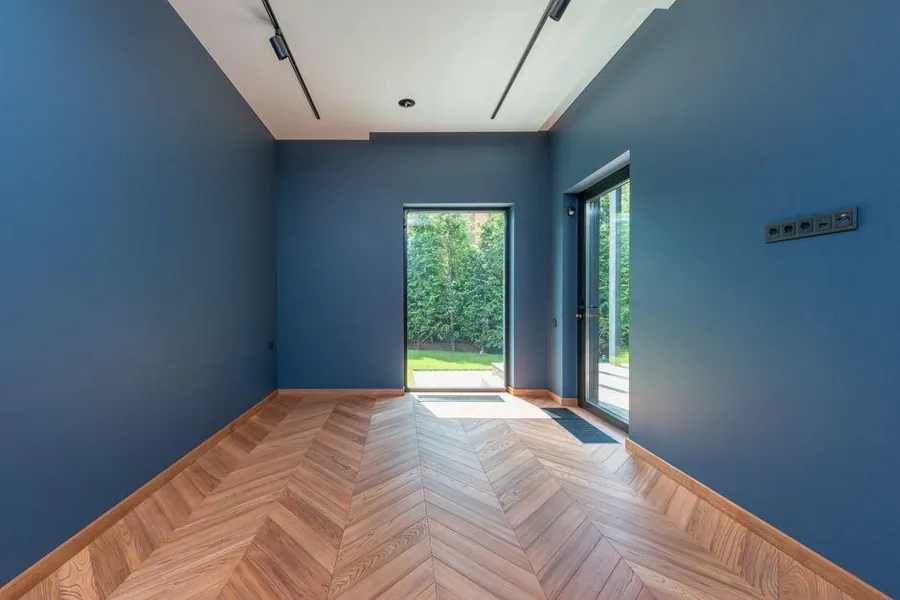 Finished garden studio interior with blue walls, herringbone timber floor and glass door opening onto the garden