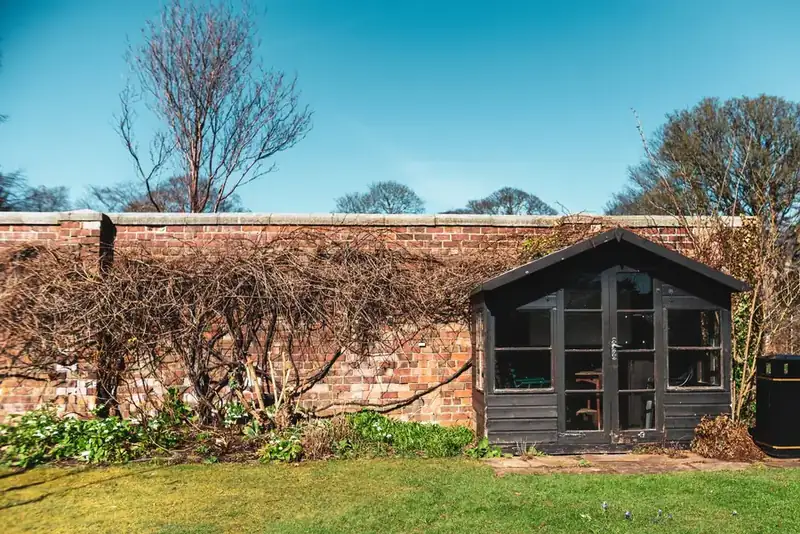 Timber garden building tucked against an old brick wall at the far end of a garden