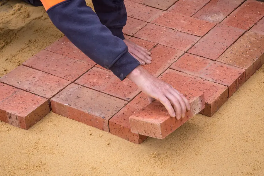 Landscaper laying block paving on a sand bed, the build stage a design fee is sometimes credited against