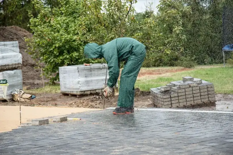 Landscaper laying block paving in the rain during a garden rebuild
