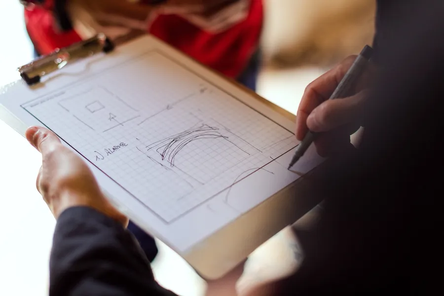Hand sketching a simple layout plan in pencil on squared paper held on a clipboard