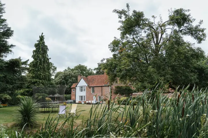 Large family garden with a trampoline, deck chairs and mature trees behind a brick house, the scale of plot that sets Harpenden build budgets