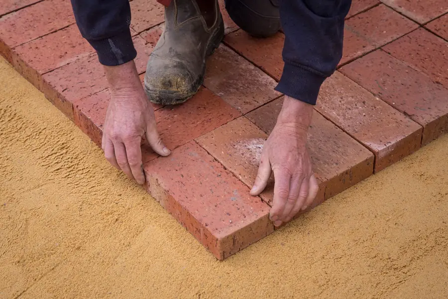 Landscaper setting red clay pavers onto a screeded sand bed, part of the hidden construction that decides how long St Albans garden paving lasts