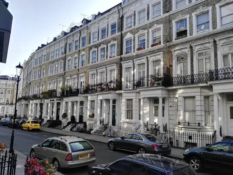 Street of tall period terraced houses with cars parked nose to tail along the kerb