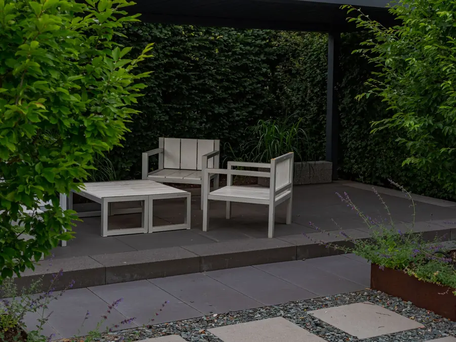 Large-format porcelain paving terrace with simple furniture against a green wall in a low-maintenance garden