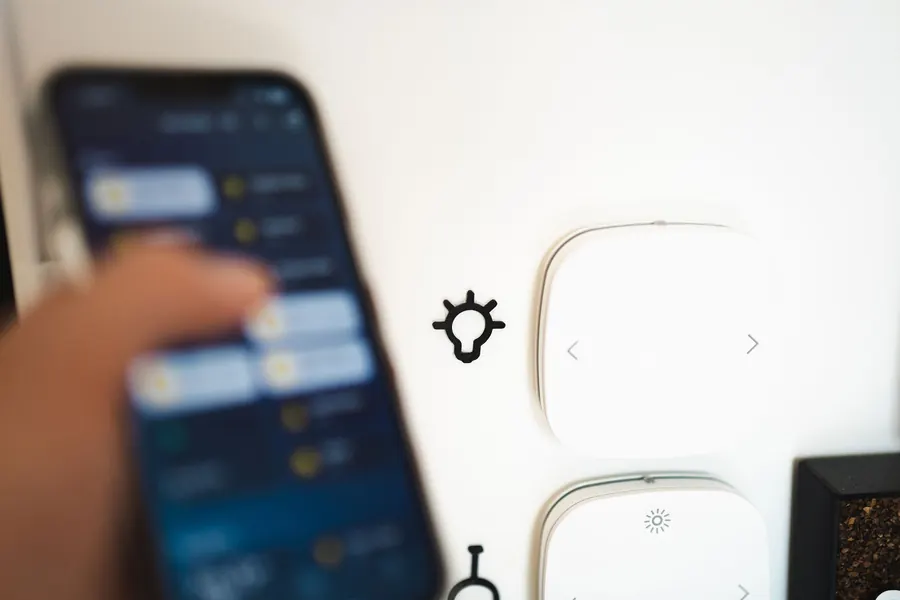 Smartphone lighting app next to wall-mounted light switches, the kind of zoned control used for a St Albans garden lighting scheme