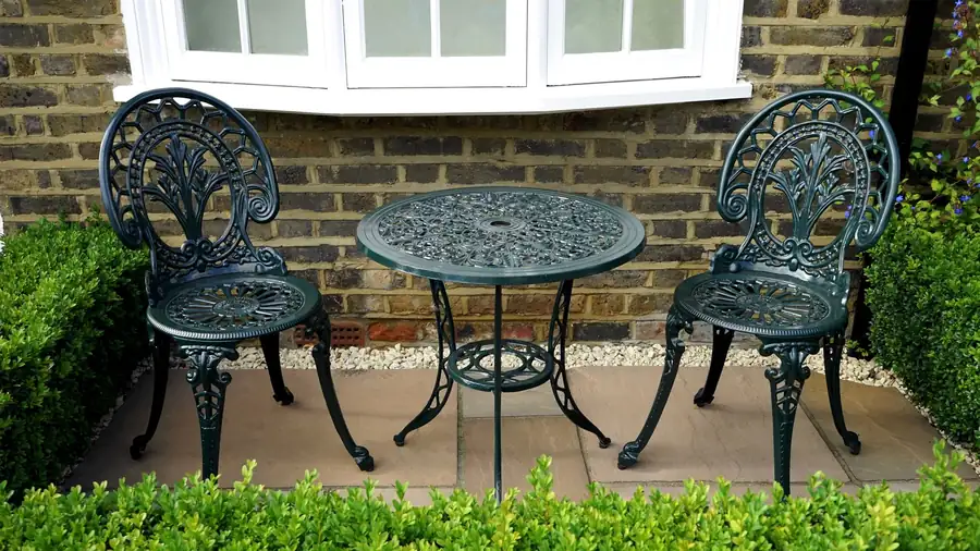 Small metal table and chairs against a brick wall beside a bay window, the tight space behind a terraced house