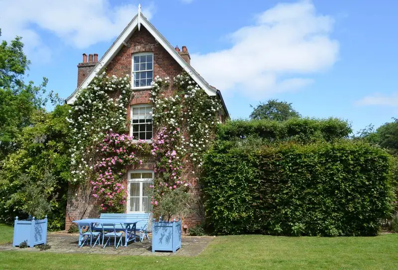 Victorian red brick house covered in climbing roses with a beech hedge and lawn, typical of a period home in a conservation area