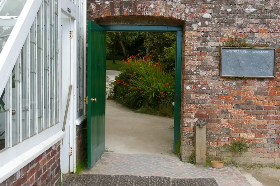 Open green door in an old brick garden wall leading to a walled garden
