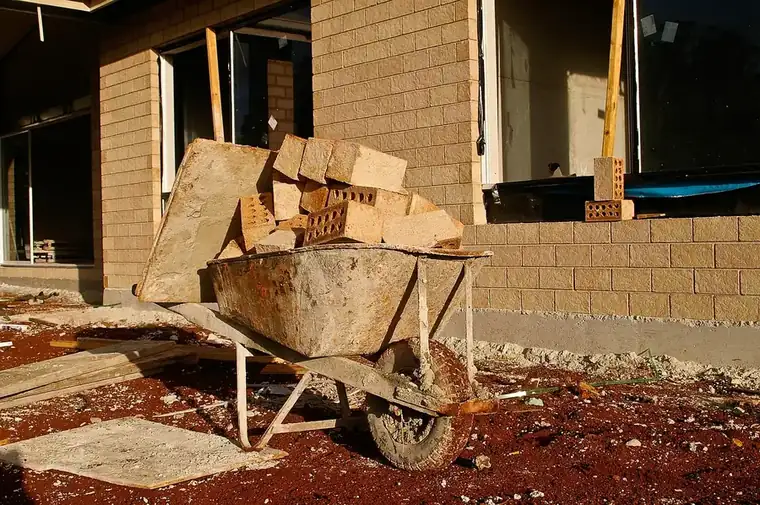 Builder's wheelbarrow piled with concrete blocks and bricks on a muddy site beside a new block wall