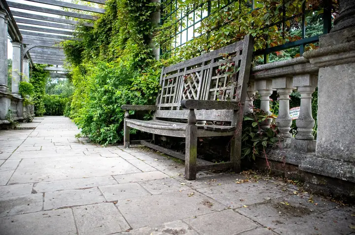 Weathered natural stone flags under a stone pergola with a timber bench and climbers, the aged York stone look many St Albans garden terraces aim for