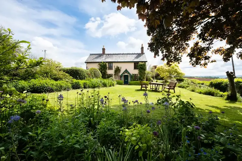 Country cottage garden with deep perennial borders and a bench looking back at the house